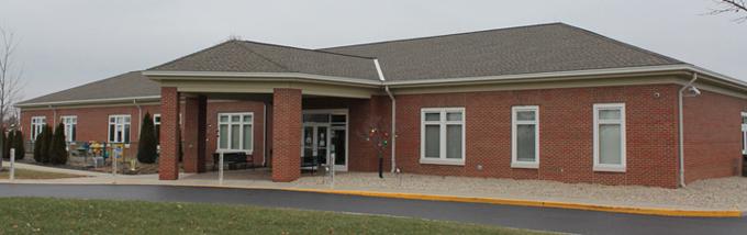 A brick building with brick columns at the entrance and tall windows and a grey roof.