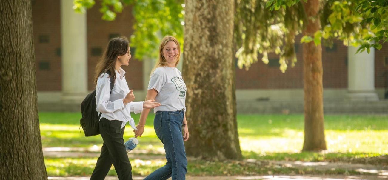 Two students walk across College Green while talking.