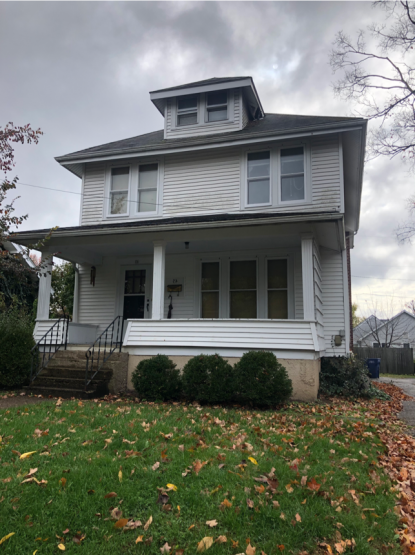 Two-story house with dormer window on attic, wood or vinyl siding, front porch and small front lawn, in a residential neighborhood