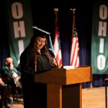 Student Bailey Ray stands in a graduation robe at a podium at commencement